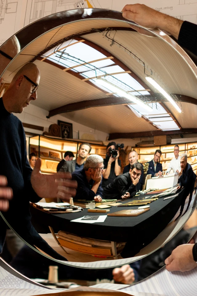 In a round witch mirror's reflection, several people are at a meeting table with prototype designs in a discussion.