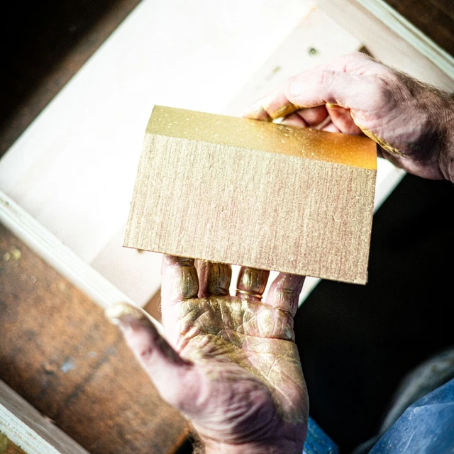 Hands holding a single shingle of the 3D golden wall panel.