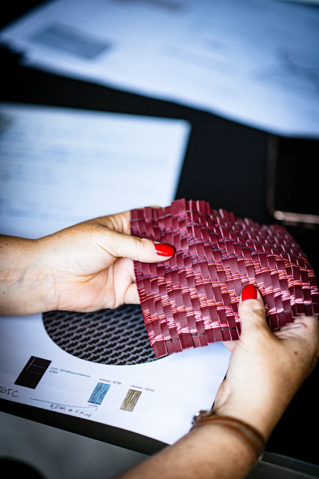 A hand holding a red woven leather patch