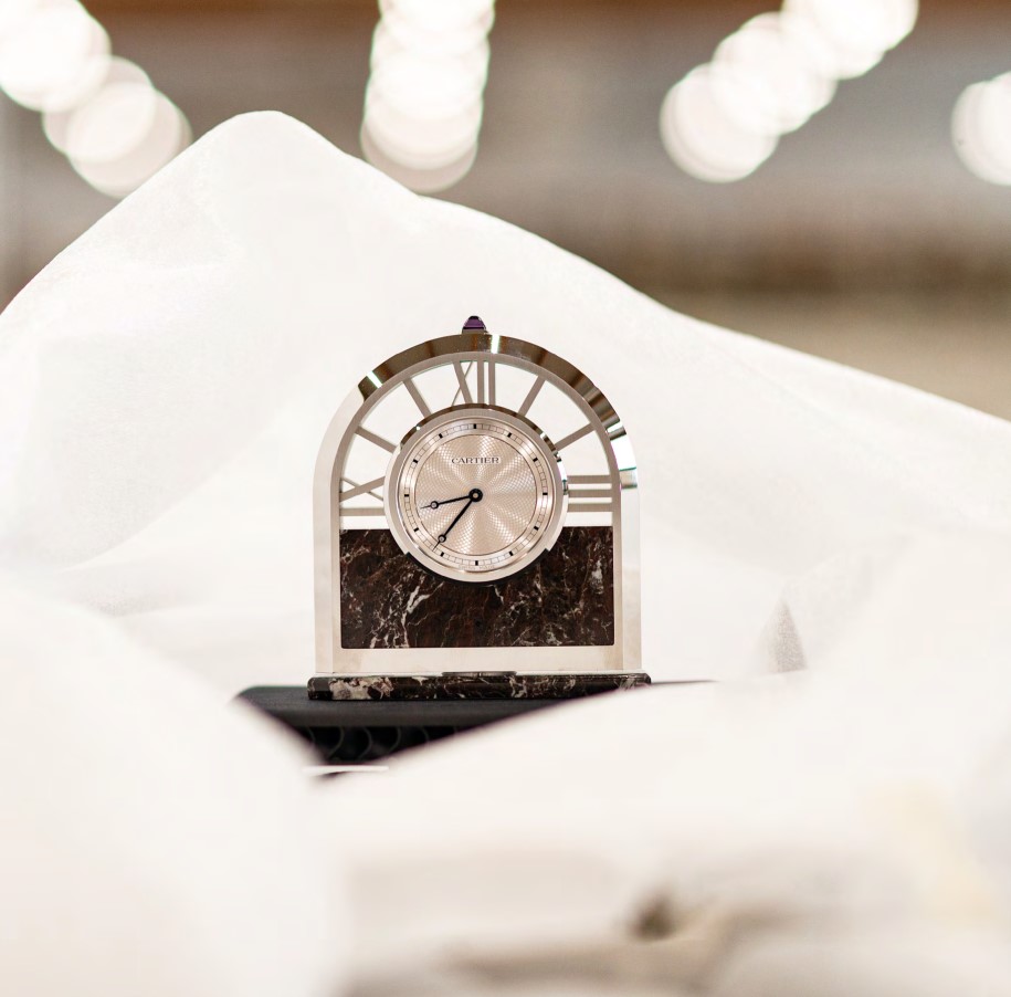 An analog cartier clock on white sheets