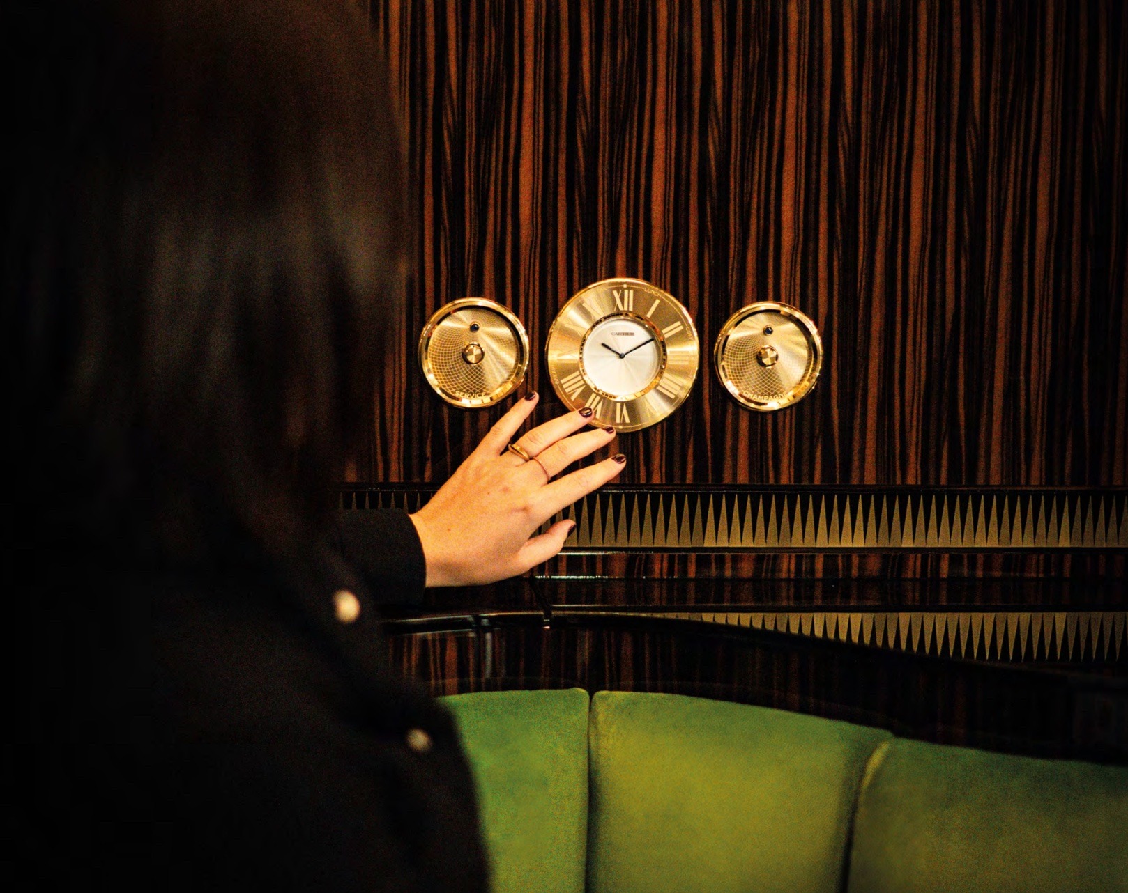 A person reaching their hands towards a gold Cartier wall-clock.