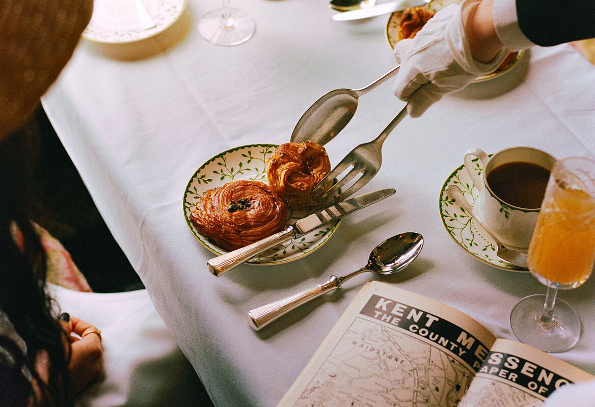 A hand serving pastries with a pair of tongs.