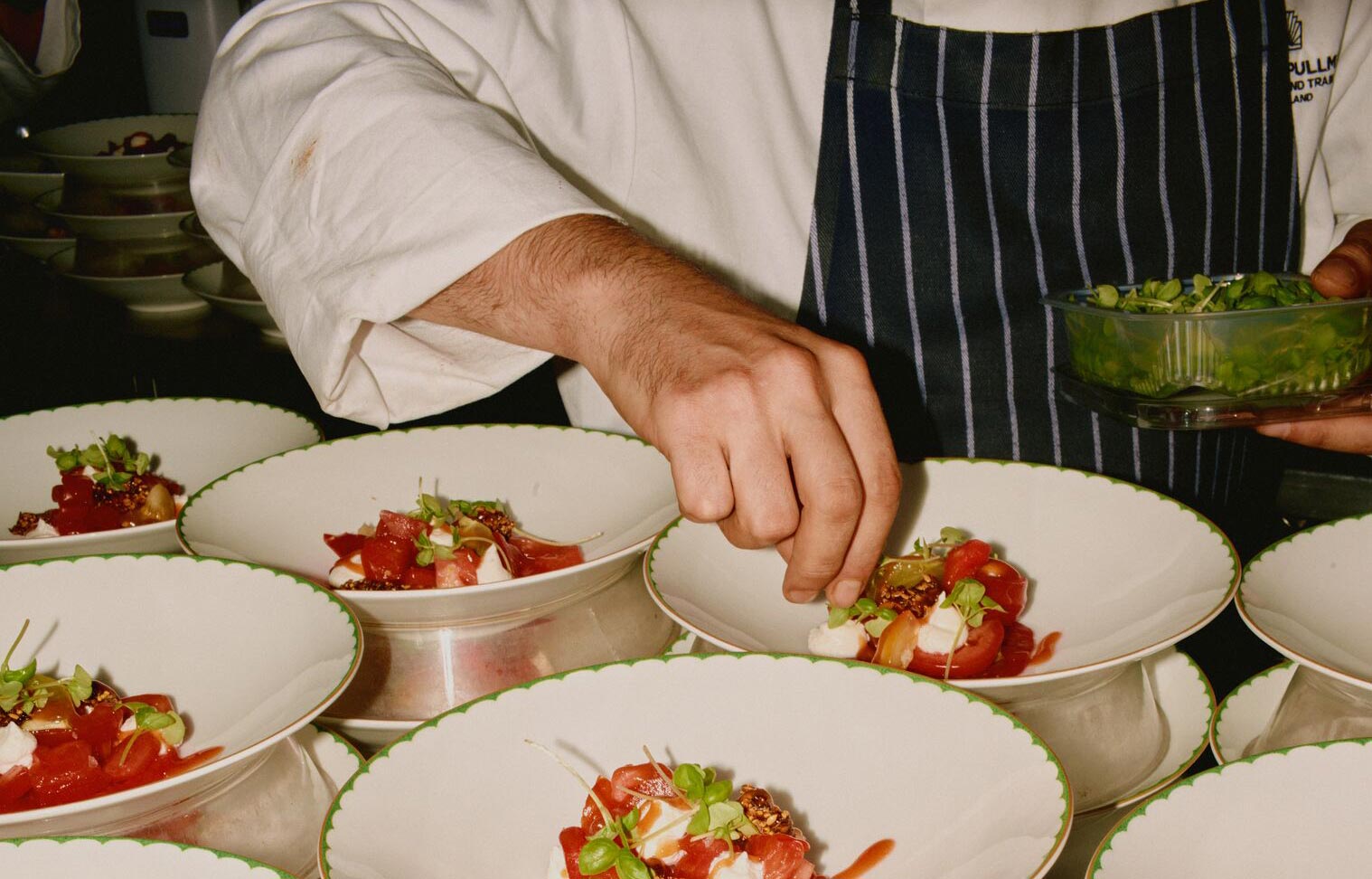 A chef, plating several dishes with garnish.