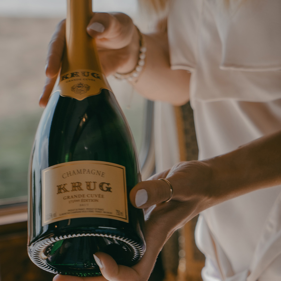 Pair of hands, holding a bottle of Krug champagne.