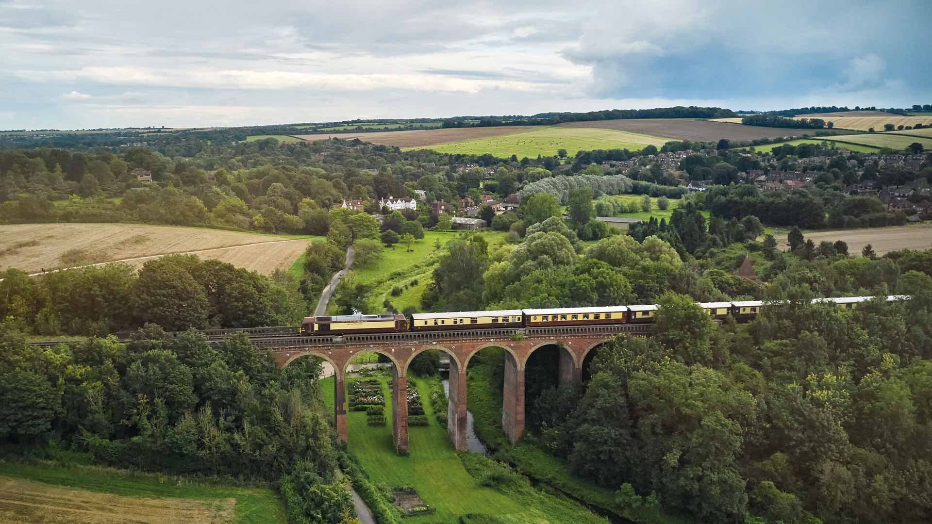 A bridge with a train crossing it over green British countryside.