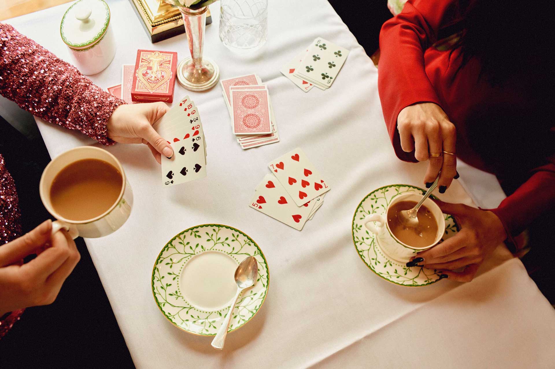 Top-down shot of two people playing cards and drinking tea.