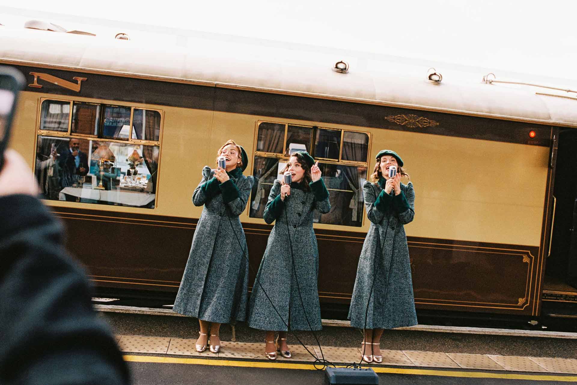 Three ladies standing on a train station platform, singing.