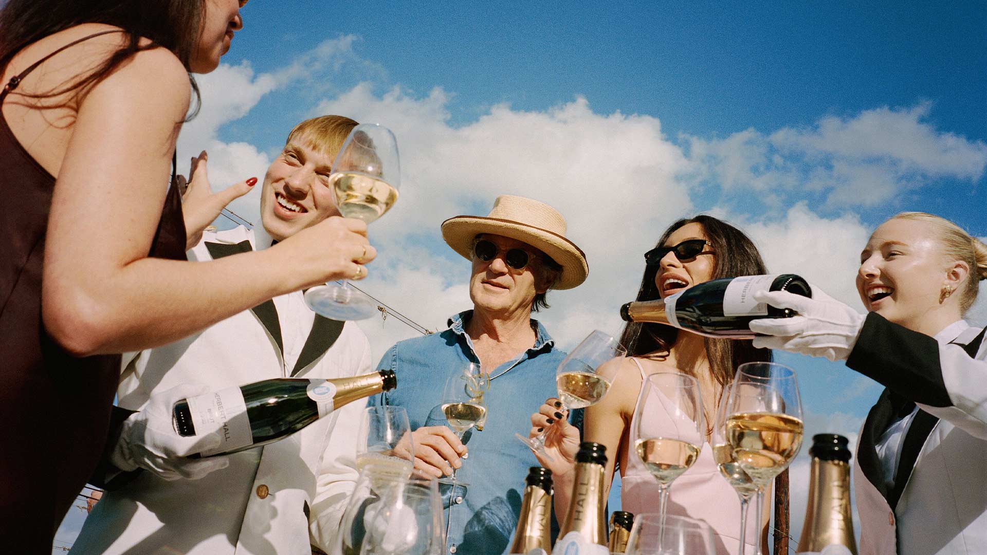 A group of people outside, drinking champagne on a clear day.