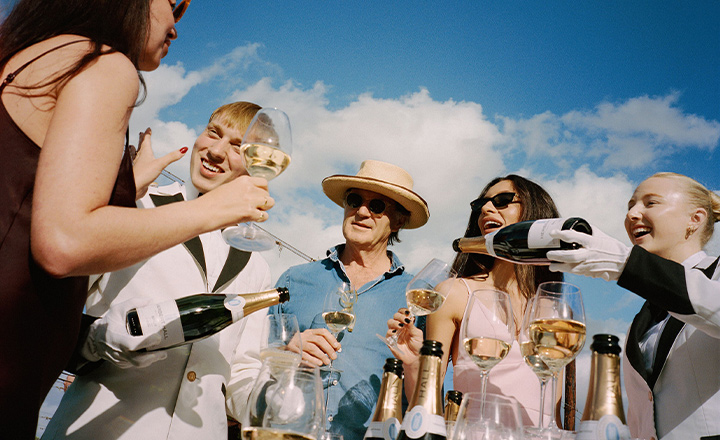 A group of people outside, drinking champagne on a clear day.