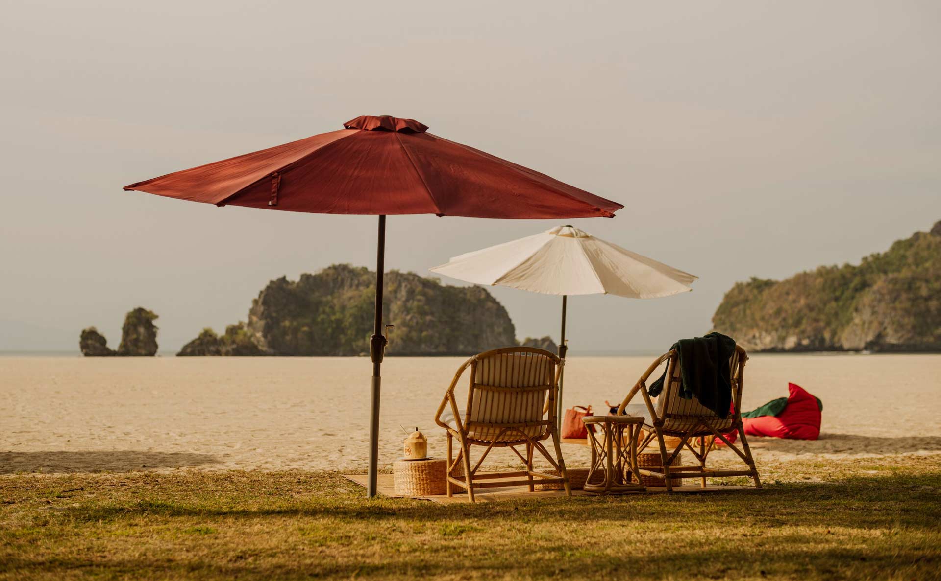 The beach. There's two chairs and a beach towel under two sun-umbrellas.