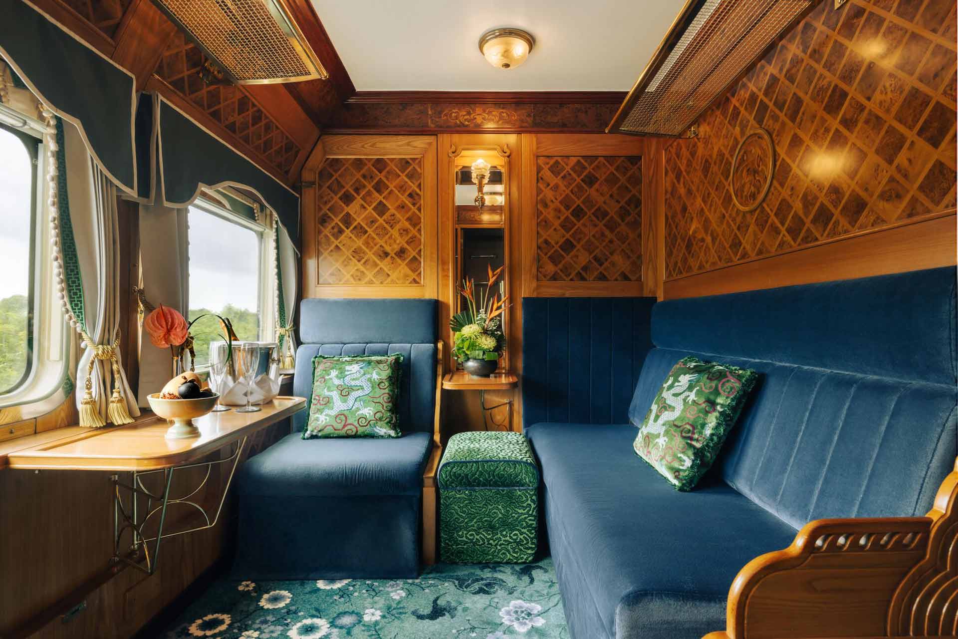 Eastern and Oriental Express' State Cabin. Daylight filters through the window onto the plush, blue settees and upholstery of the seating.