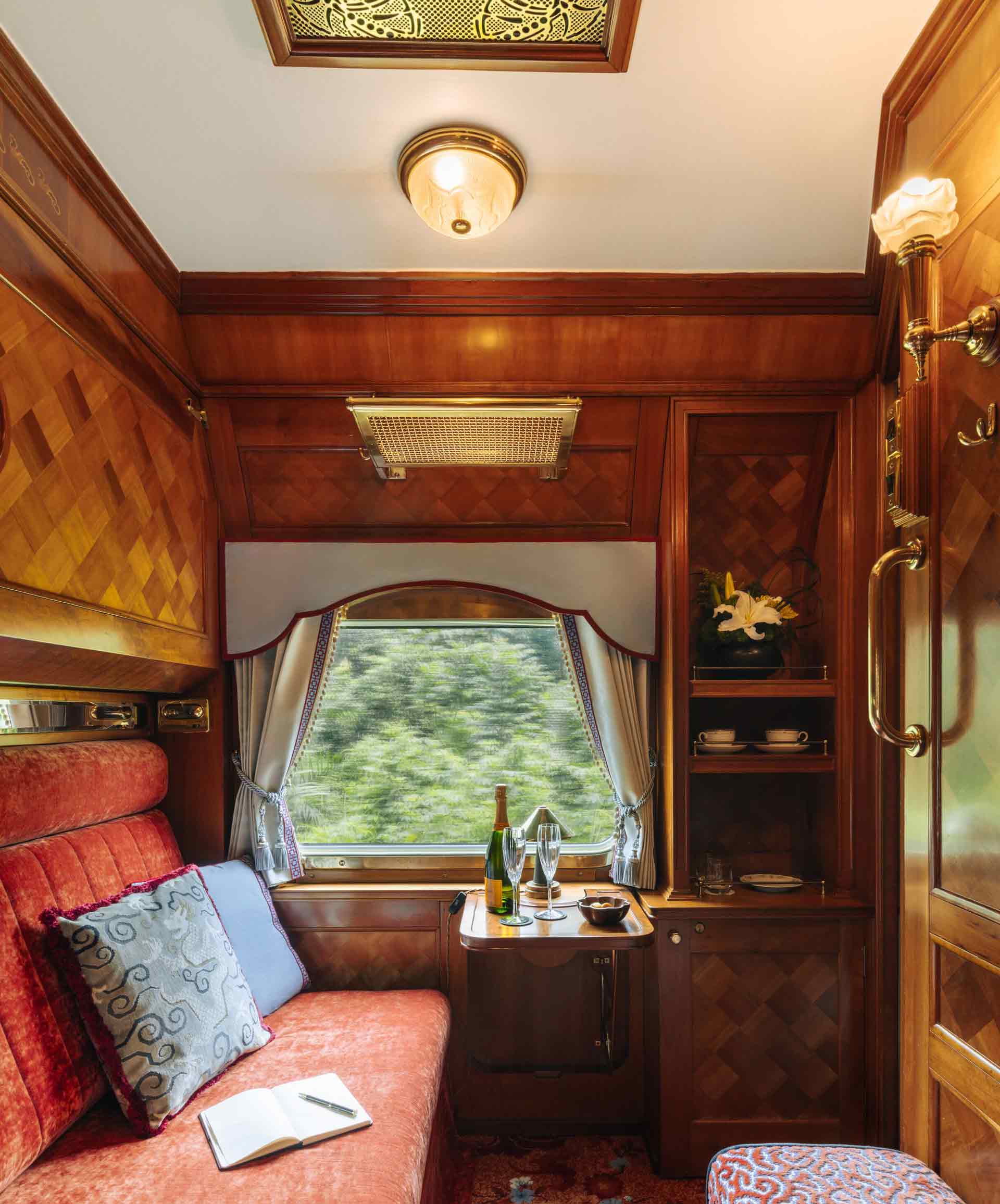Eastern and Oriental Express' Pullman Cabin by day, visible is the red velvet seting and a small stowaway-table with wine and snacks.