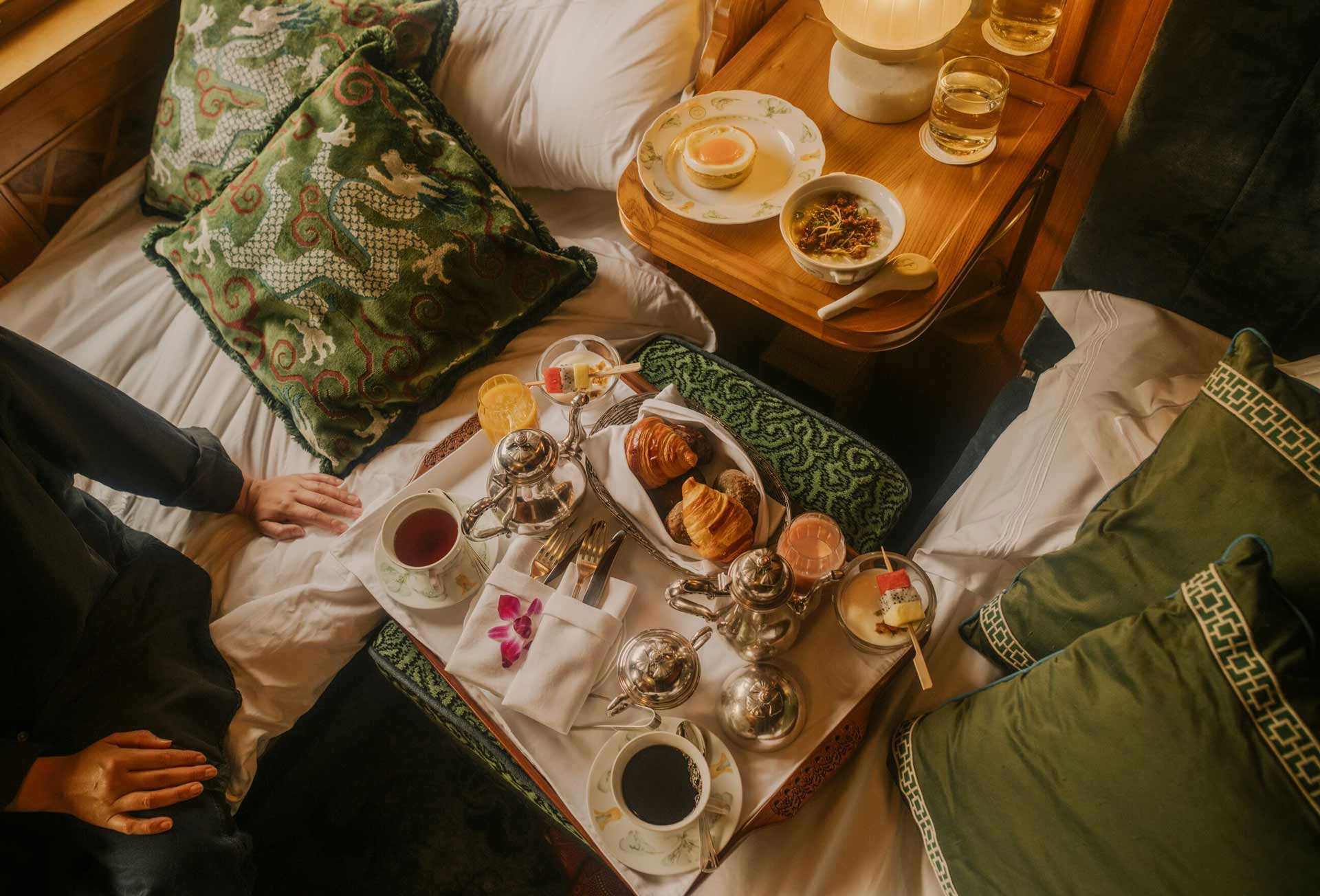 An elegant continental breakfast spread, served on trays, on a bed.