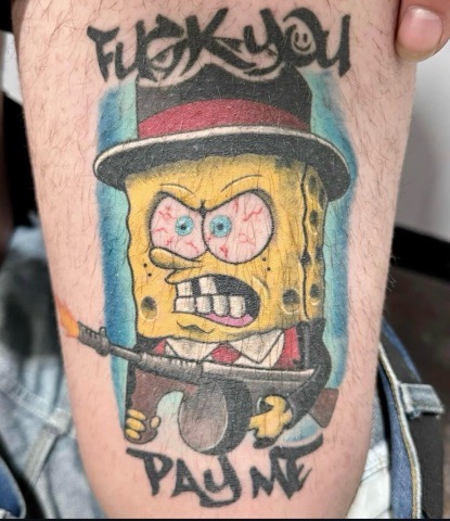 Tattoo on skin of an angry SpongeBob SquarePants character wearing a black and red hat and suit, holding a rifle, with the words 'FUCK YOU' above and 'PAY ME' below.