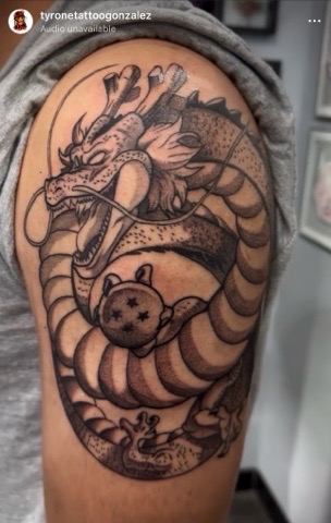 Black and grey tattoo of a fierce, coiled Chinese-style dragon with detailed scales, whiskers, and claws covering a person's upper arm.