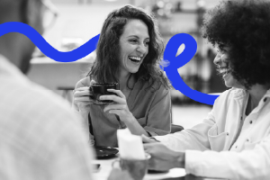 Three diverse people laughing and enjoying coffee together at a café table.
