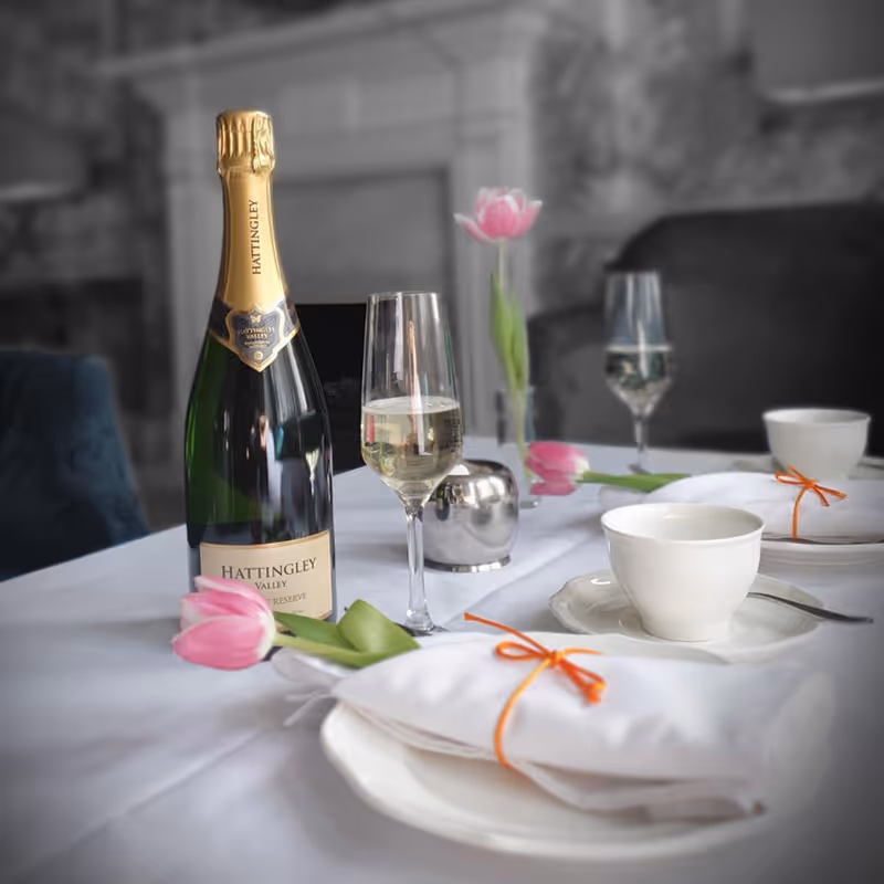 Bottle and two glasses of wine with two ceramic teacups and plates with tulips wrapped in napkins.