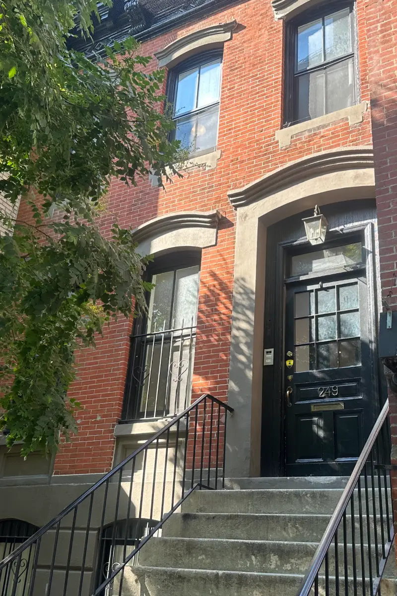 Exterior of a red-brick townhouse with a black front door and stone steps