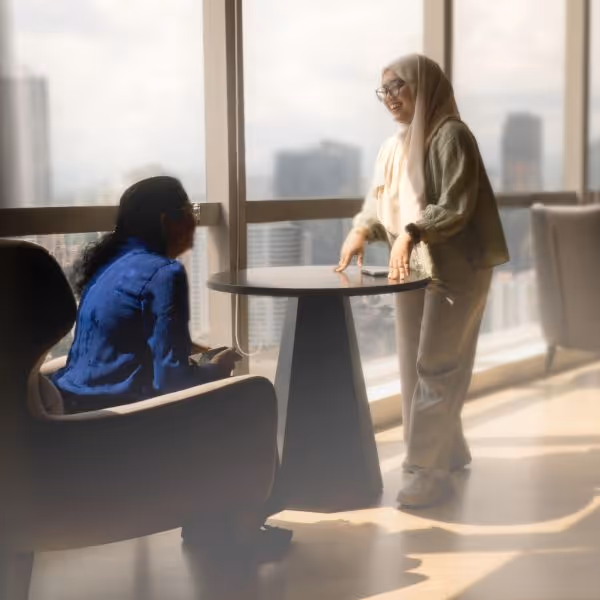 Our team in Kuala Lumpur - woman sits at table whilst a second woman stands in front of her smiling.