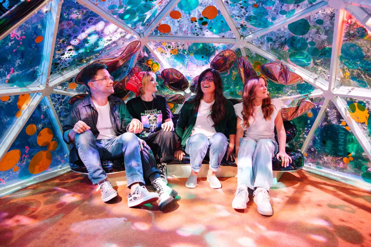 A group of four people are sitting inside a colorful geodesic dome at Meow Wolf Grapevine