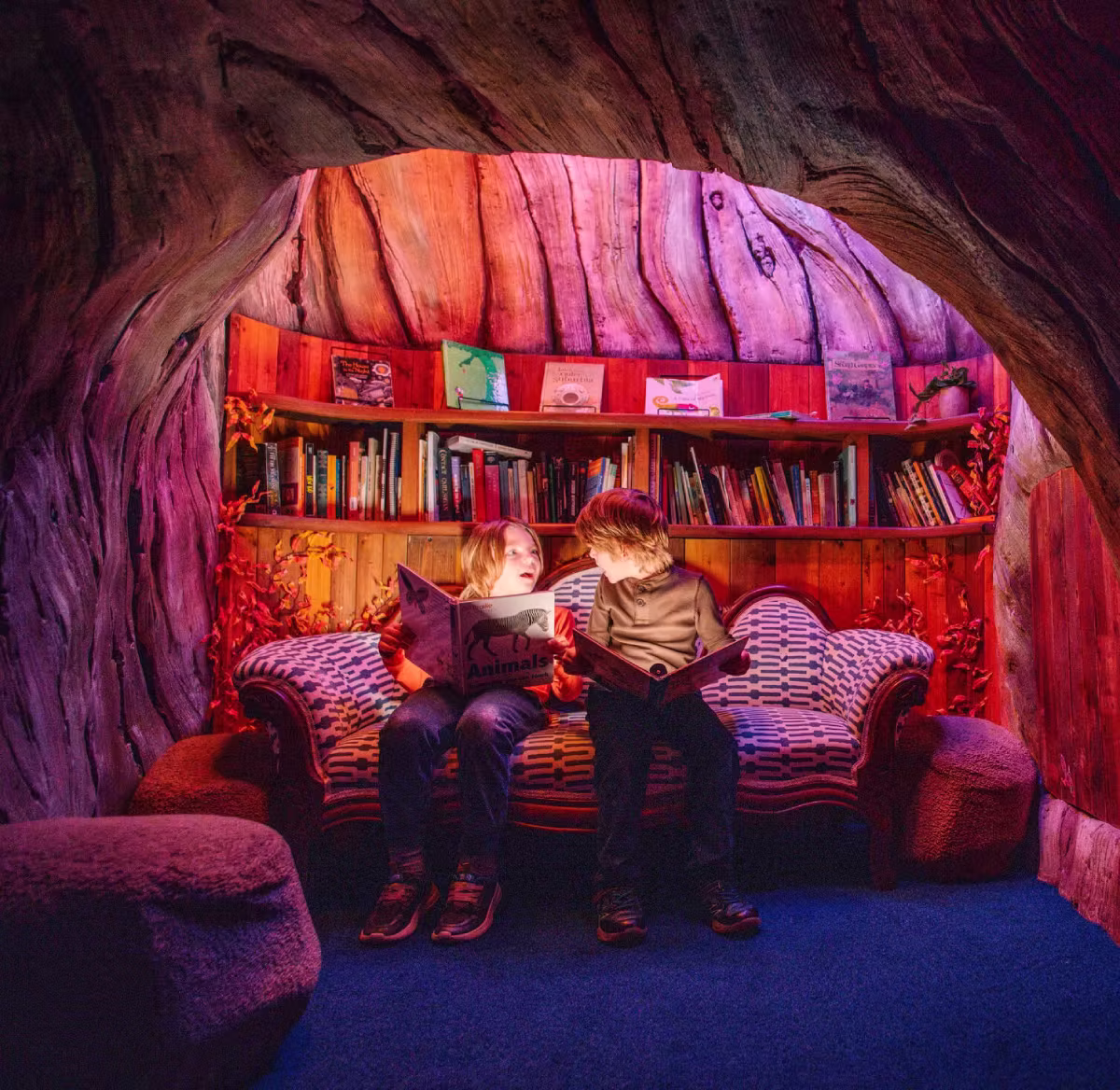 Two children reading books inside a hollowed trunk of an imaginary tree.