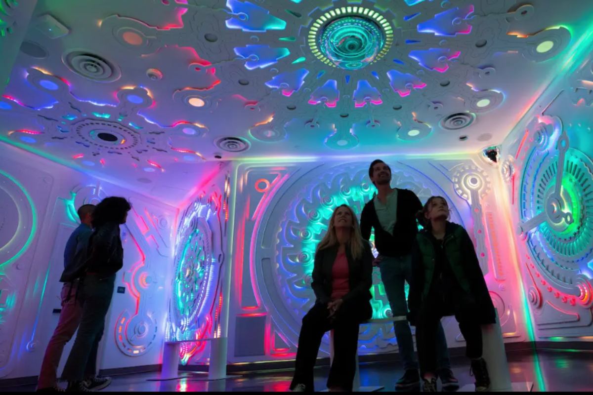 Two groups of people gather in a white room with multicolor lit cutouts.