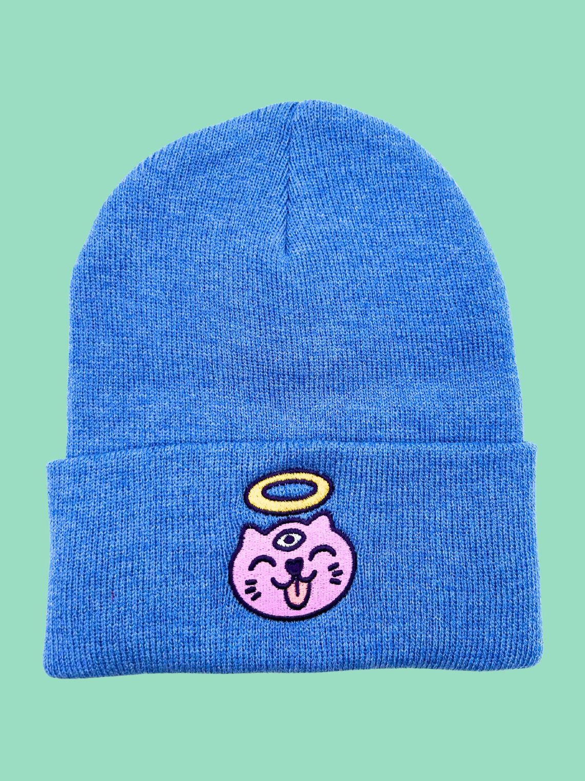 A picture of a blue beanie with a three-eyed cat with a halo above its head.