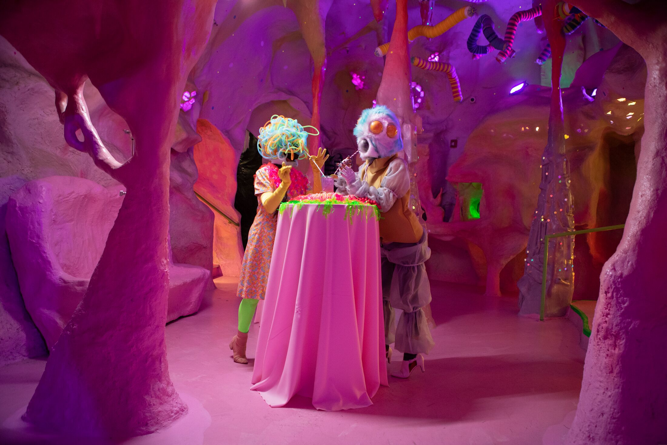 two interdimensional beings at a table with drinks in a pink cave