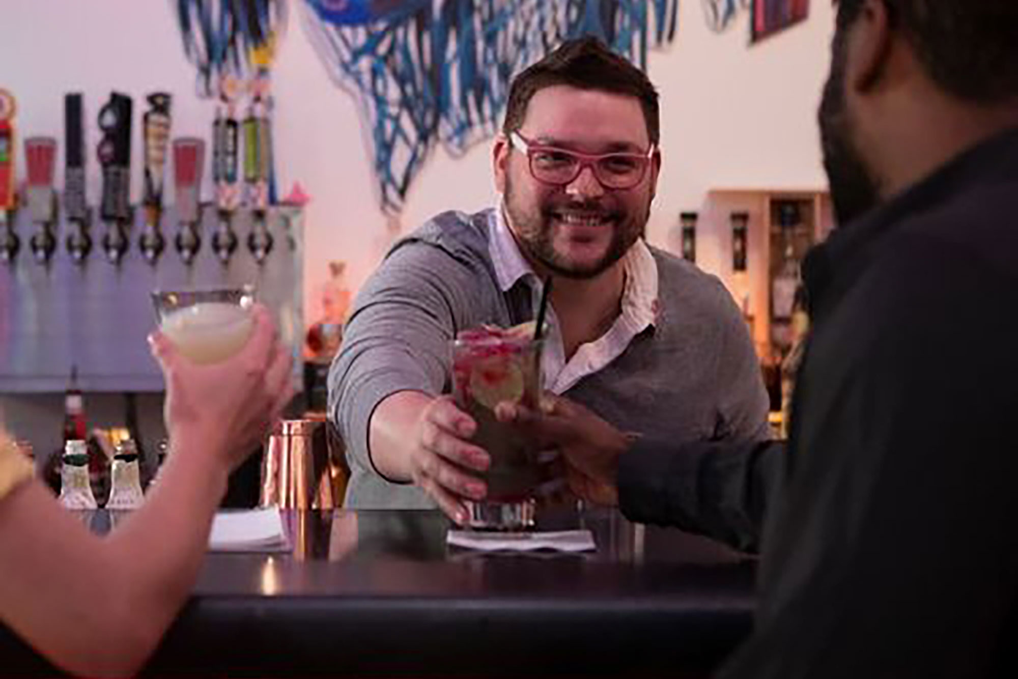 person with short dark hair and glasses handing a drink to a person
