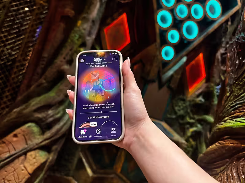 hand holding phone with Meow Wolf Psychic Sensor up against a forest background