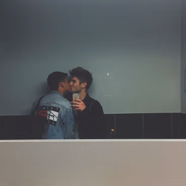 A couple taking a mirror selfie of them kissing one another. 