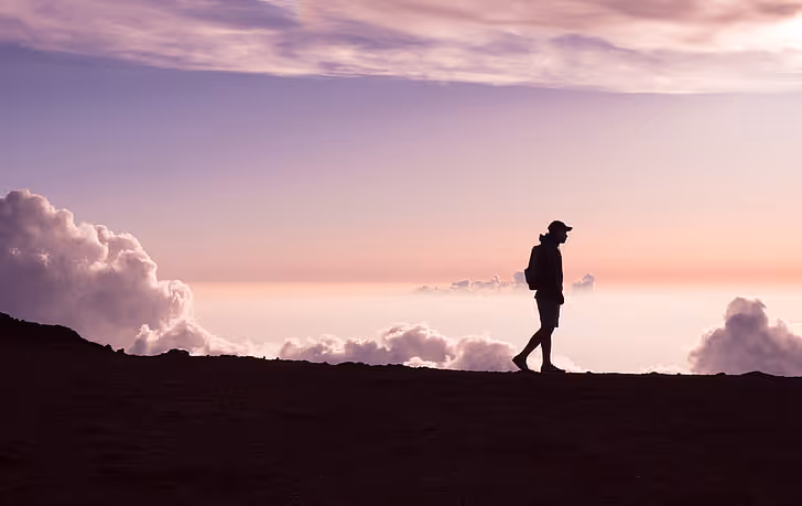 An individual walking with the sky behind them. 