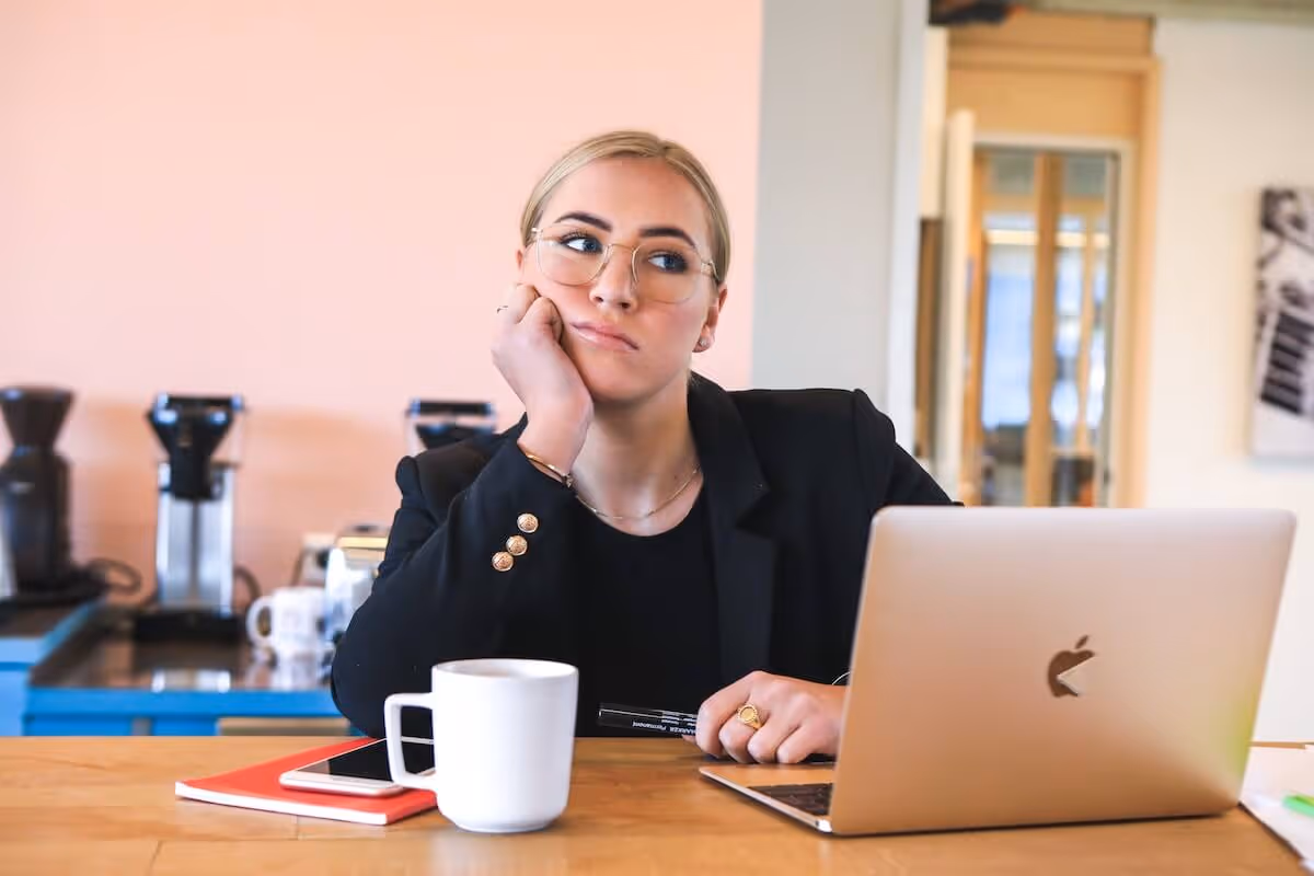 Woman sits at her desk behind a laptop with an unhappy face