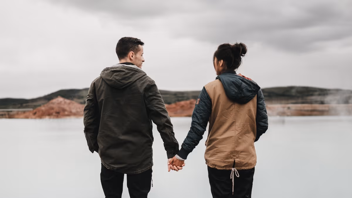 Couple standing in front of a lake, holding hands, looking at one another