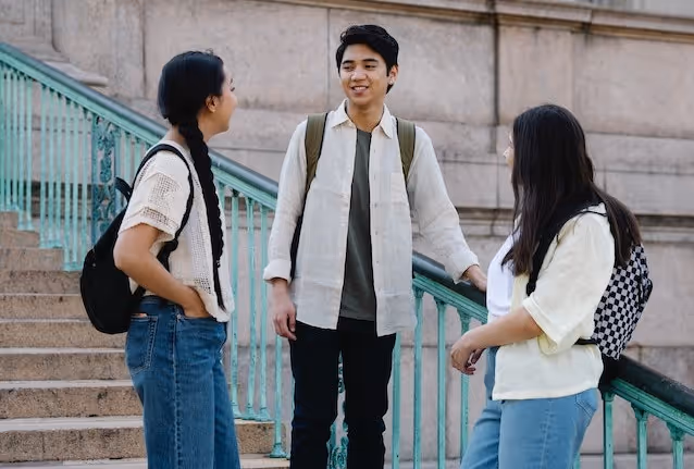 Three new peers stand on a set of stairs at their university, answering icebreaker questions.