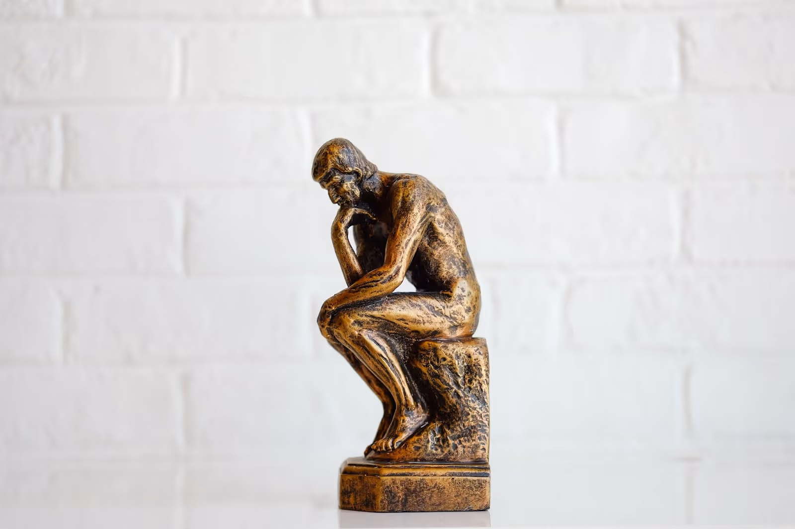 A small bronze book end replica of the statue of “The Thinker” sits on a white shelf