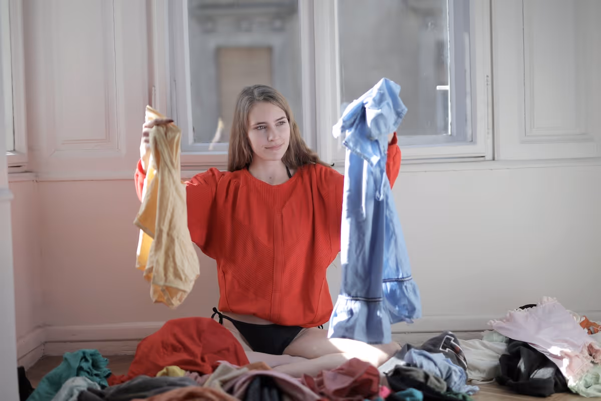 A woman holding and inspecting two items of clothes. ‍
