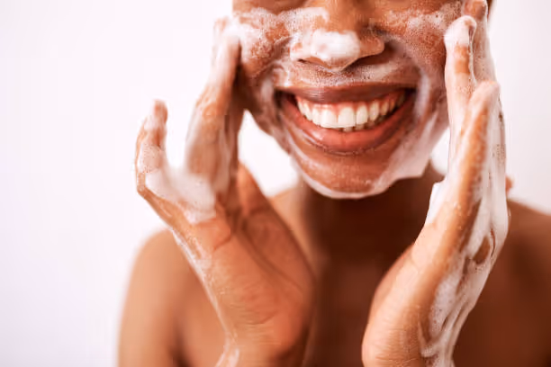 A Black girl smiling while washing her face.Â