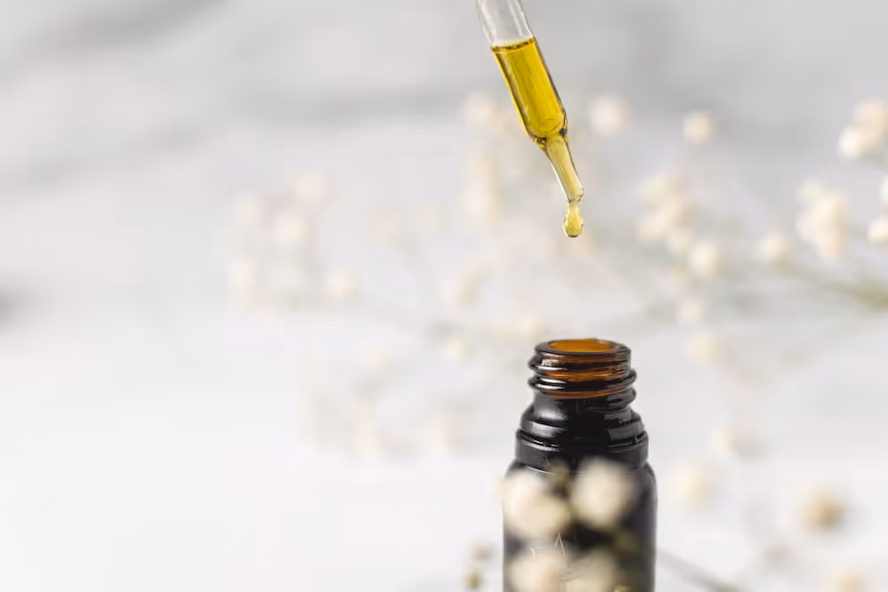 A dropper is dropping a yellow liquid into an unlabeled bottle.