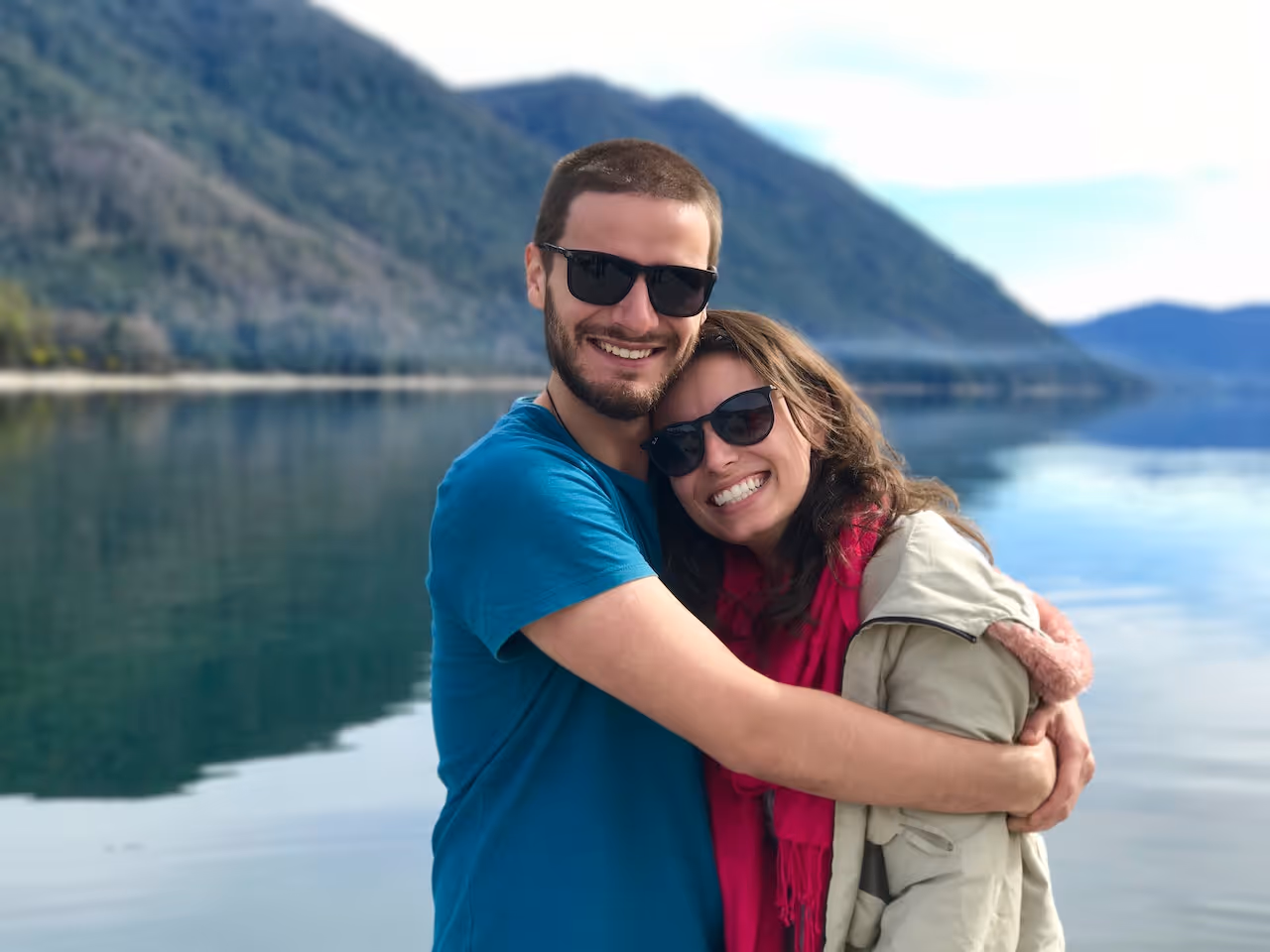 man and woman embracing in front of a mountain lake