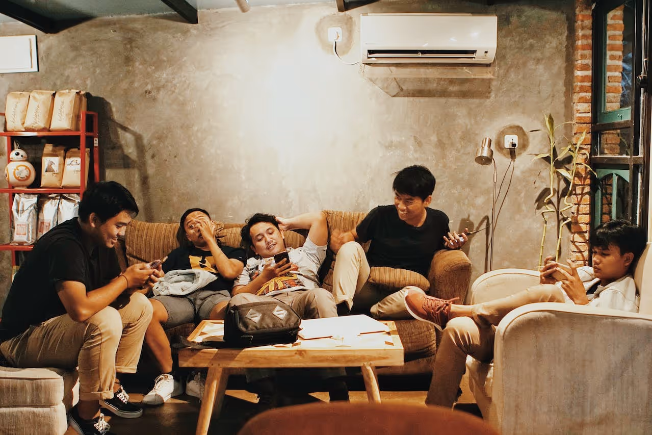 group of five friends hanging out in a living room texting and talking