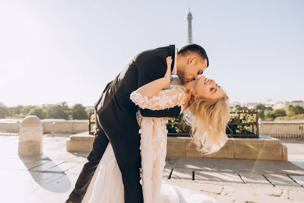 man in suit dipping woman in wedding dress and kissing her neck in front of the eiffel tower