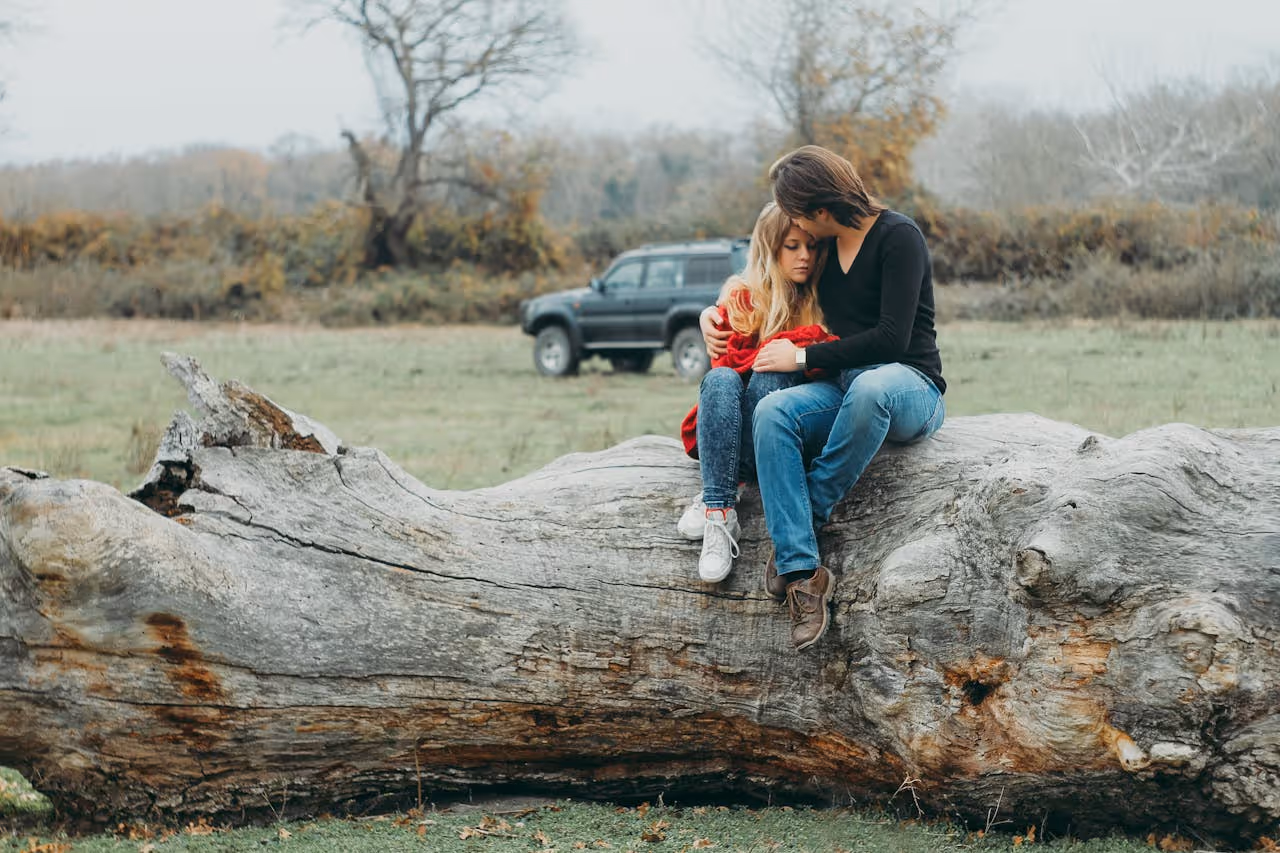 man sitting on large piece of driftwood comforting his daughter