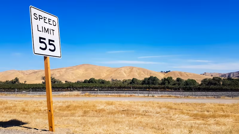A speed limit sign on a road with mountains in back.