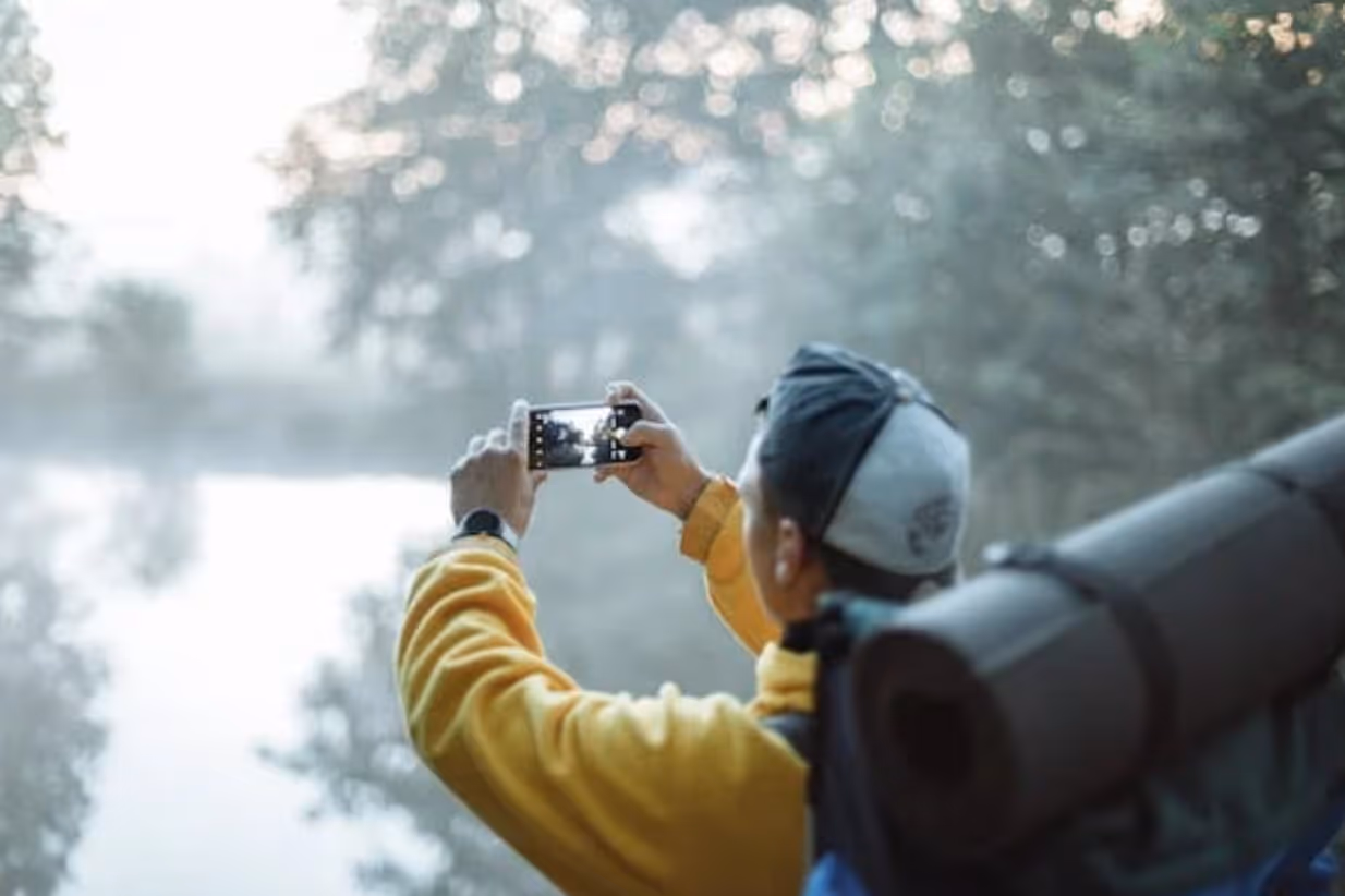 A man captures a scenic river view with his camera, focusing intently on the natural beauty before him.  