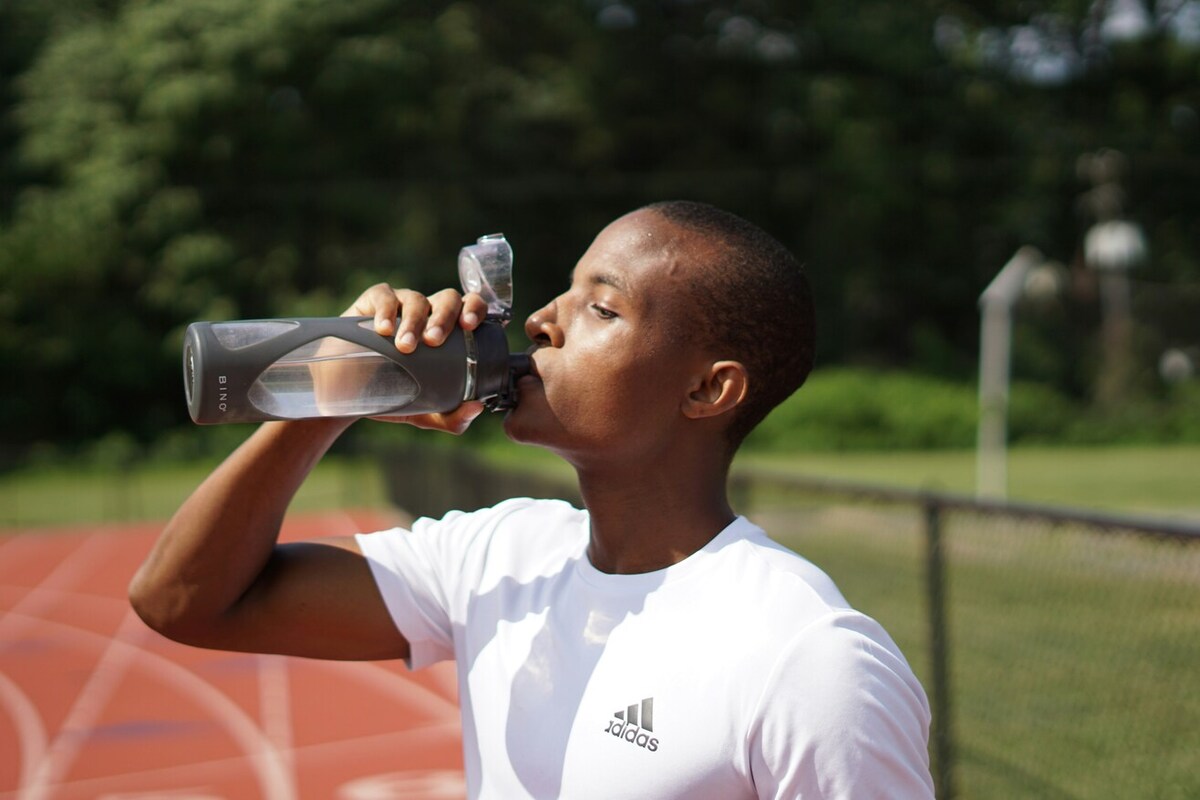 A person on a sports track drinking from a water bottle.