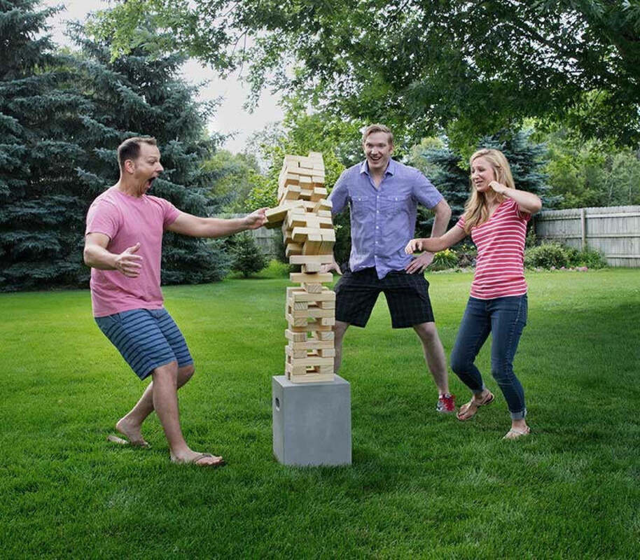 Three people standing around a tower of wooden blocks as it falls.