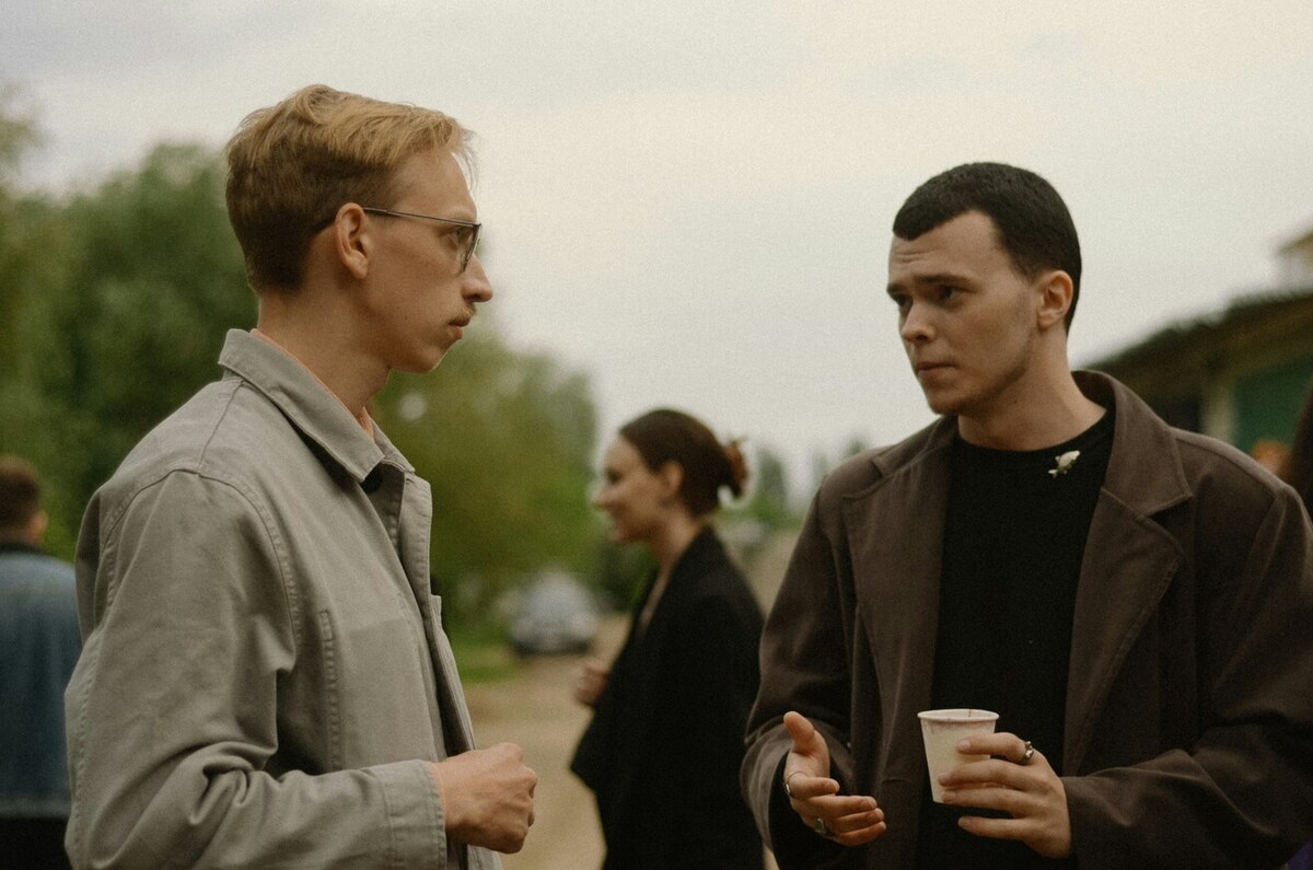 Two people speaking to each other. One holds a paper cup.