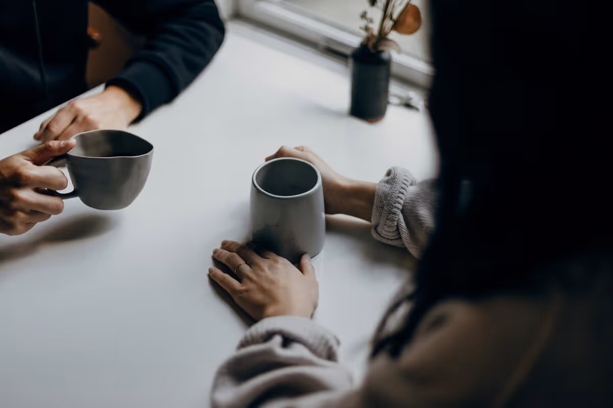 Two people having a conversation. They each hold a cup of coffee, which is the focus of the photo.