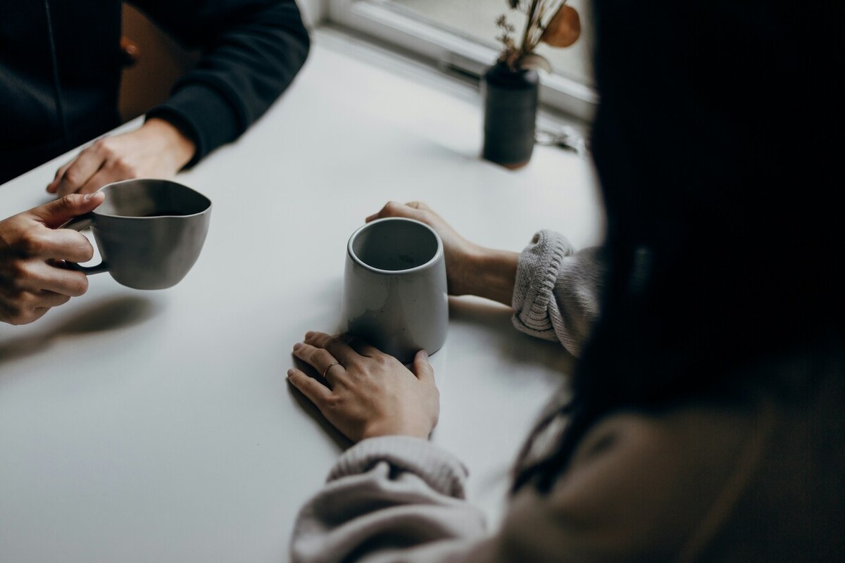 Two people having a conversation. They each hold a cup of coffee, which is the focus of the photo.